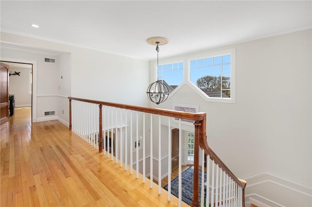 hallway featuring a healthy amount of sunlight, wood finished floors, a chandelier, and visible vents