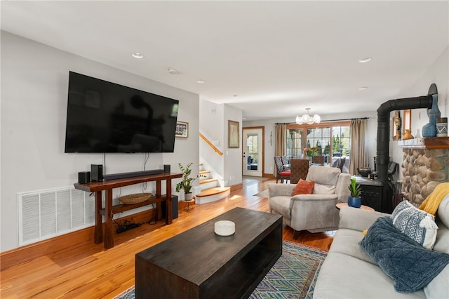 living room featuring stairs, a chandelier, light wood-style floors, a wood stove, and visible vents