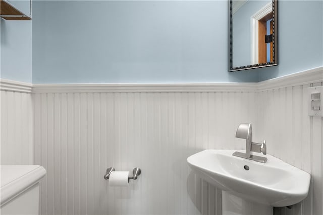 bathroom with toilet, a wainscoted wall, and a sink