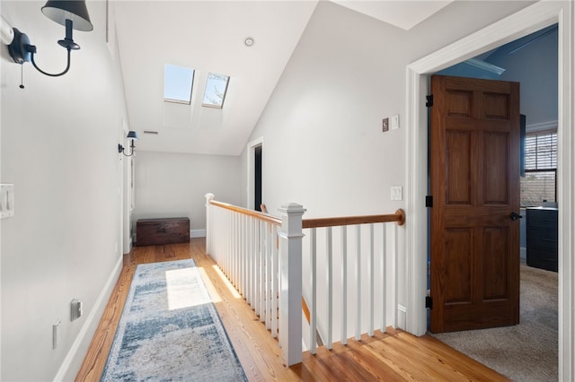 hallway featuring vaulted ceiling with skylight, wood finished floors, baseboards, and an upstairs landing