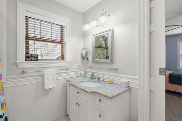 bathroom with wainscoting, a healthy amount of sunlight, vanity, and tile walls