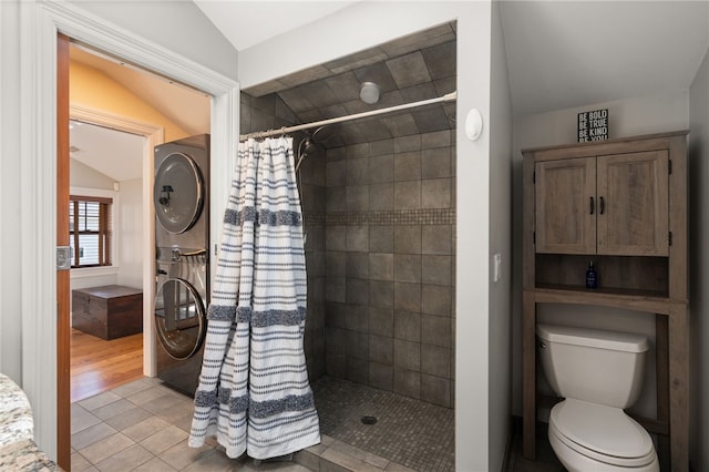 bathroom with lofted ceiling, toilet, stacked washer / dryer, and tiled shower