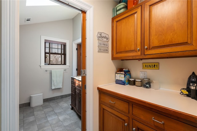 kitchen featuring lofted ceiling, light countertops, visible vents, baseboards, and brown cabinetry