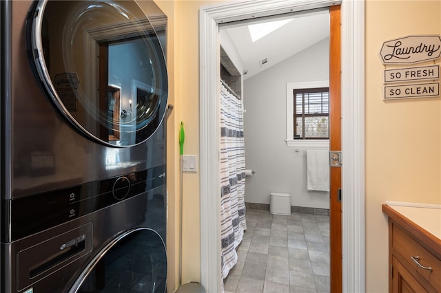 laundry area with a skylight, light tile patterned flooring, stacked washer / drying machine, baseboards, and laundry area