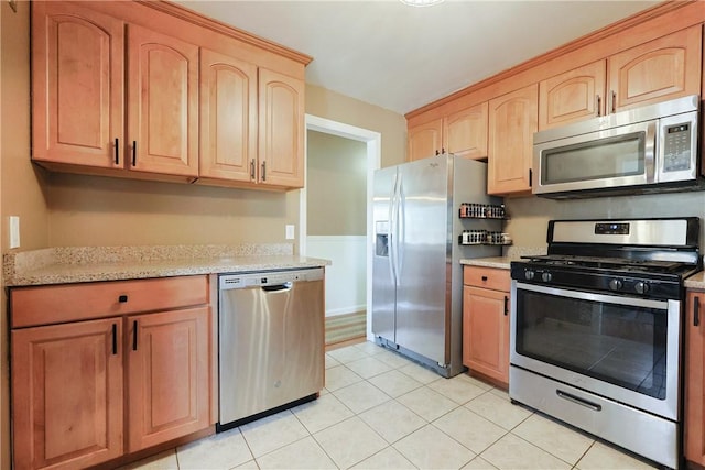 kitchen with light brown cabinetry, light stone countertops, stainless steel appliances, and light tile patterned floors