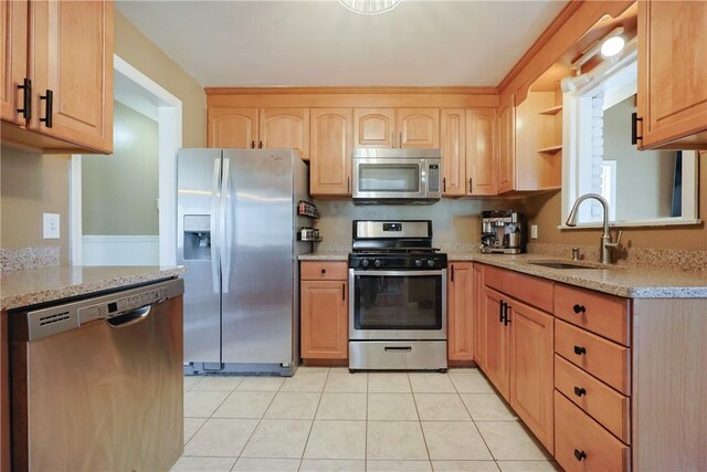 kitchen featuring a sink, appliances with stainless steel finishes, light stone countertops, light brown cabinets, and light tile patterned floors