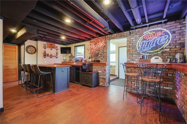 bar with wood finished floors, brick wall, and bar
