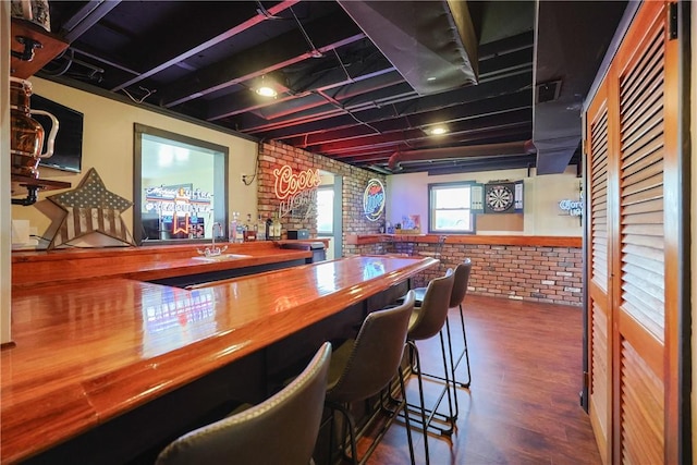 bar with wood finished floors, a bar, and brick wall