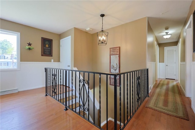 hall featuring a notable chandelier, baseboard heating, wood finished floors, and an upstairs landing