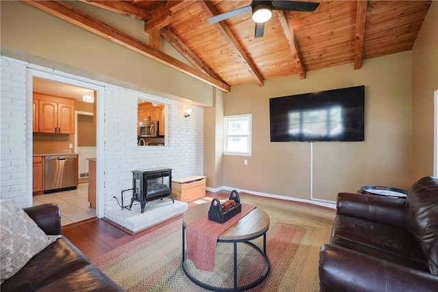 living room with light wood-style flooring, vaulted ceiling with beams, a ceiling fan, wood ceiling, and a wood stove
