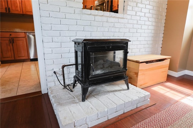 room details featuring dishwasher, baseboards, a wood stove, and wood finished floors