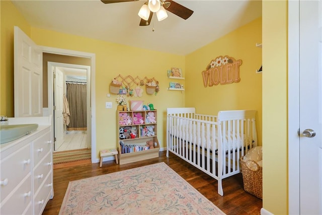 bedroom featuring a nursery area, ceiling fan, a sink, and dark wood-style floors