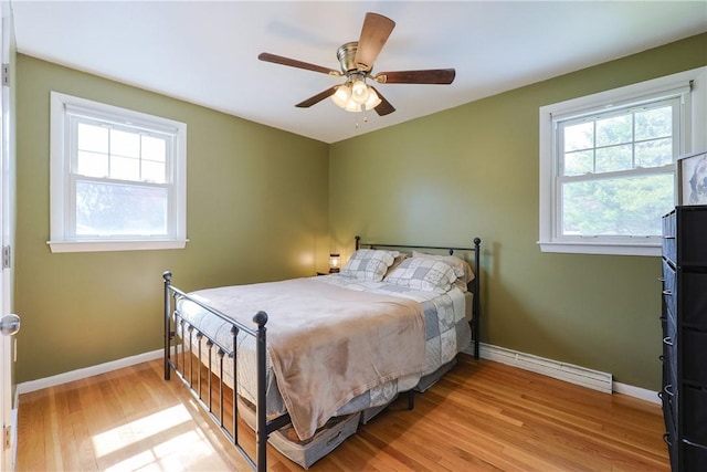 bedroom with light wood finished floors, baseboards, a baseboard radiator, and multiple windows