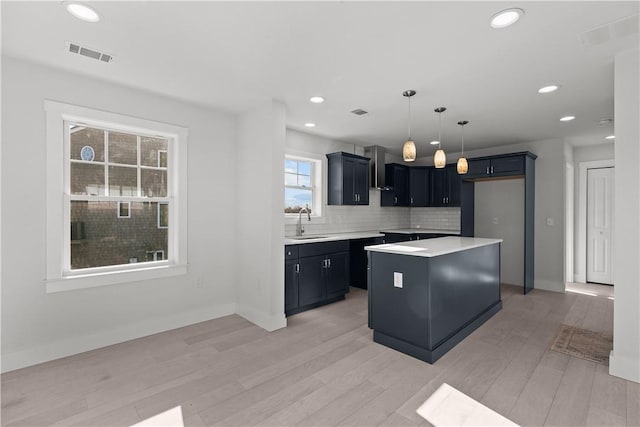 kitchen with visible vents, a sink, light wood-style floors, a center island, and decorative backsplash