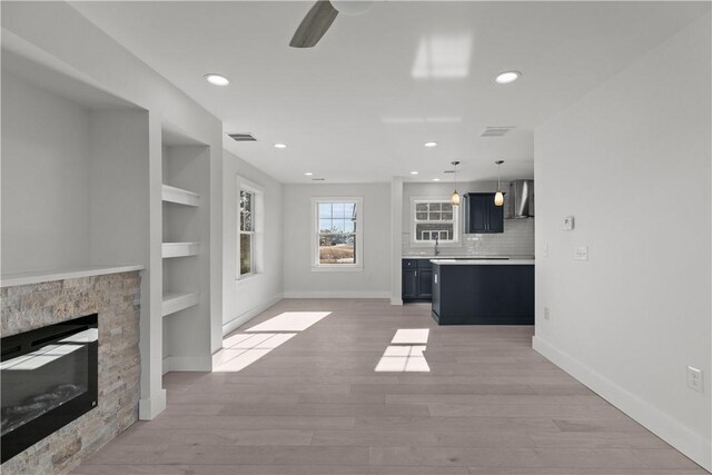 unfurnished living room featuring a stone fireplace, light wood-type flooring, baseboards, visible vents, and recessed lighting