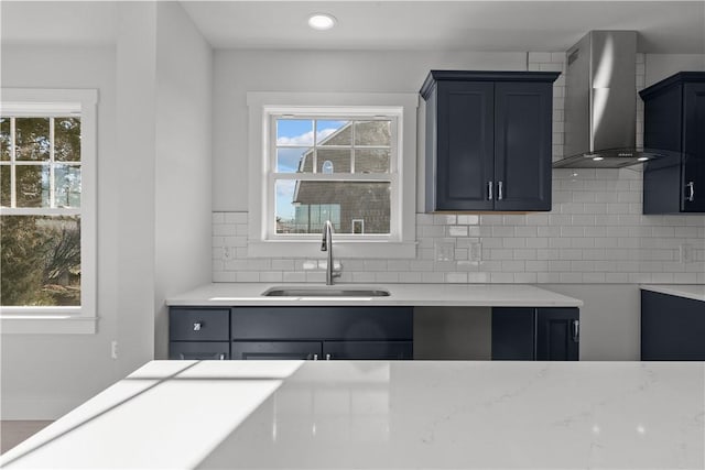 kitchen featuring a sink, recessed lighting, backsplash, wall chimney range hood, and light countertops