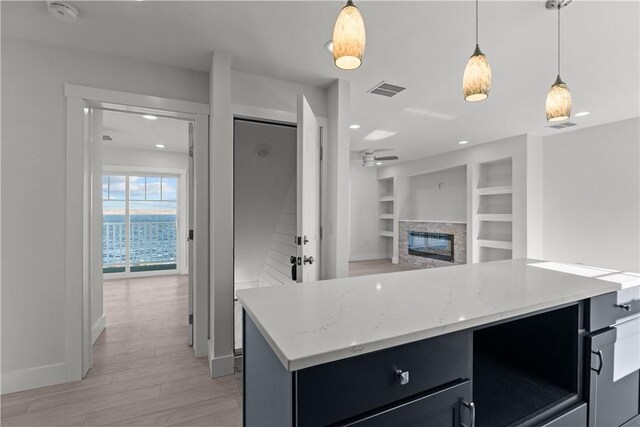 kitchen with light wood-type flooring, baseboards, built in shelves, a ceiling fan, and a fireplace