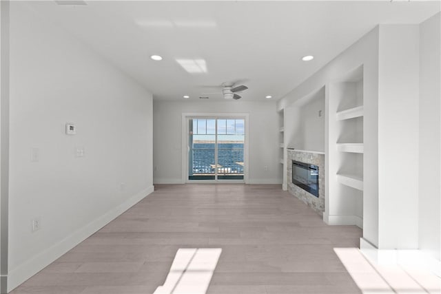 unfurnished living room with light wood-type flooring, baseboards, a glass covered fireplace, recessed lighting, and a ceiling fan
