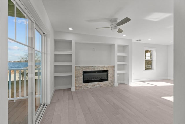 unfurnished living room with wood finished floors, a ceiling fan, baseboards, a fireplace, and built in shelves