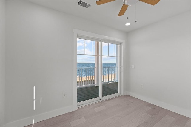 unfurnished room featuring a water view, light wood-type flooring, baseboards, visible vents, and a ceiling fan