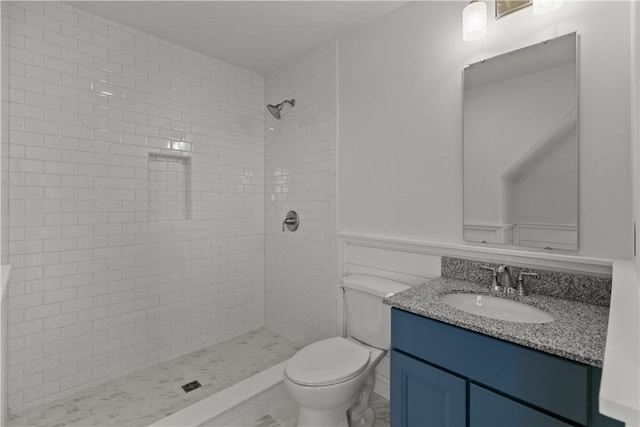 bathroom with wainscoting, tiled shower, vanity, and toilet