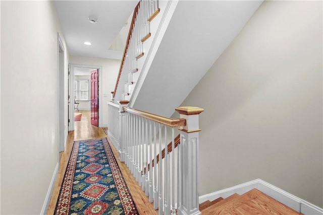 hallway with light wood finished floors, baseboards, recessed lighting, and an upstairs landing