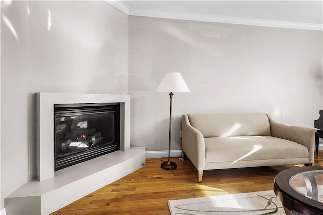 living room featuring a glass covered fireplace, baseboards, wood finished floors, and ornamental molding