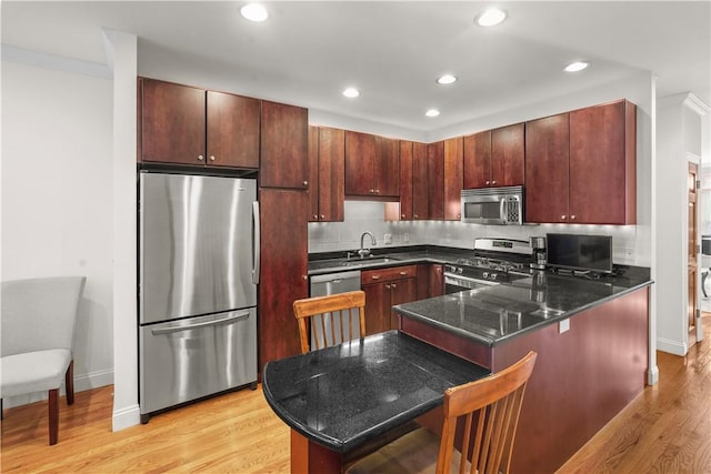 kitchen featuring light wood-type flooring, a peninsula, a sink, and appliances with stainless steel finishes