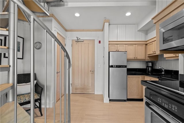 kitchen featuring light brown cabinetry, a sink, light wood-type flooring, dark countertops, and appliances with stainless steel finishes