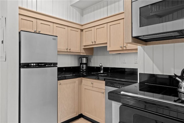 kitchen featuring dark countertops, appliances with stainless steel finishes, a sink, and light brown cabinetry