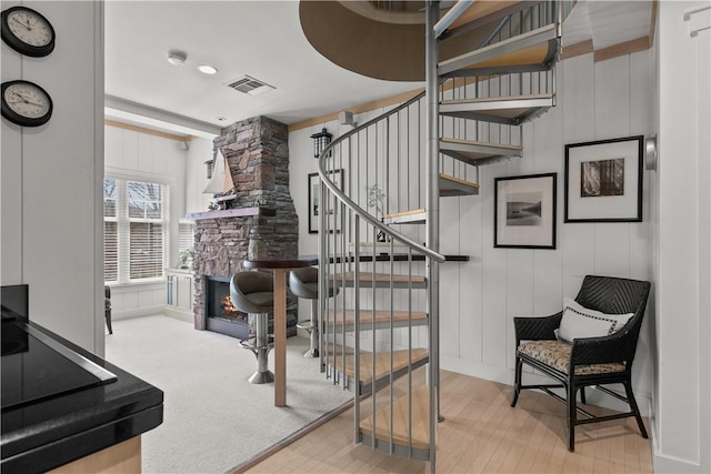 stairway featuring wood finished floors, visible vents, and a fireplace