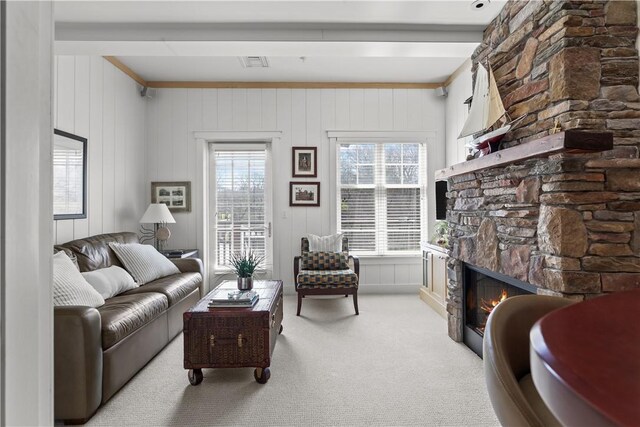 living area featuring a stone fireplace, visible vents, and carpet