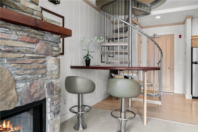 bar featuring stairway, wood finished floors, freestanding refrigerator, a fireplace, and carpet flooring