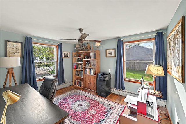home office featuring baseboards, ceiling fan, a baseboard heating unit, and wood finished floors