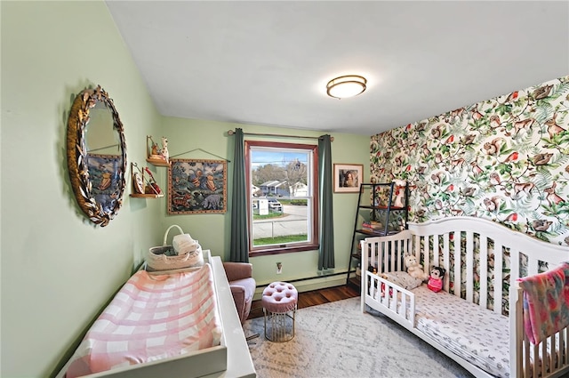 bedroom featuring wood finished floors, a nursery area, and baseboard heating
