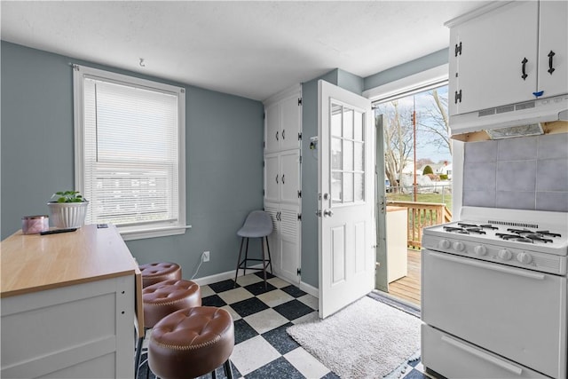 kitchen featuring tile patterned floors, baseboards, white gas stove, light countertops, and under cabinet range hood