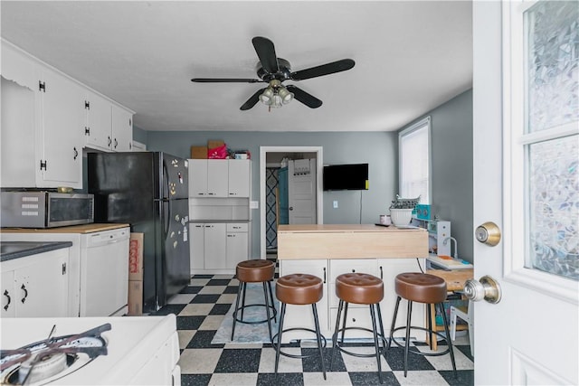 kitchen featuring dark floors, dishwasher, a ceiling fan, stainless steel microwave, and white cabinetry
