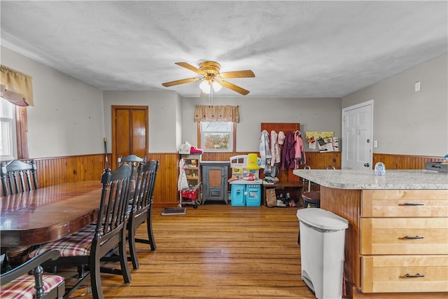 dining room with light wood-style floors, wood walls, ceiling fan, and wainscoting