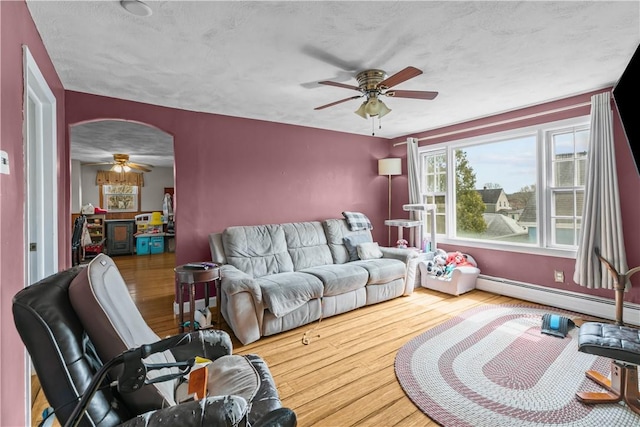 living area featuring arched walkways, wood finished floors, baseboard heating, and ceiling fan