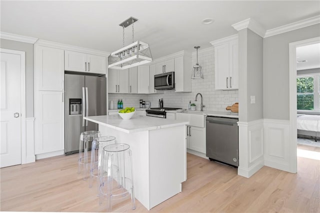 0 Greenwich Blvd Unit 203, East Greenwich, RI 02818 - kitchen with stainless steel appliances, a sink, light wood-style floors, a kitchen breakfast bar, and crown molding