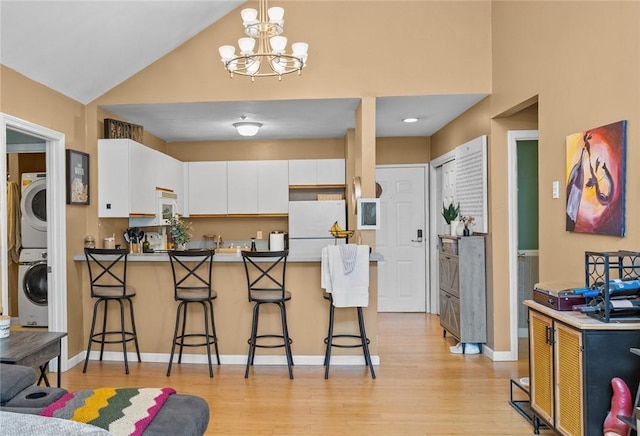 kitchen featuring a breakfast bar area, light wood finished floors, a peninsula, stacked washer and clothes dryer, and freestanding refrigerator