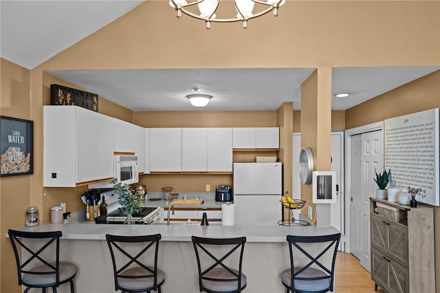 kitchen featuring a breakfast bar, white appliances, light countertops, white cabinets, and a peninsula