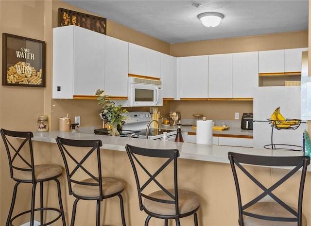 kitchen with white cabinets, a peninsula, white appliances, and a breakfast bar area