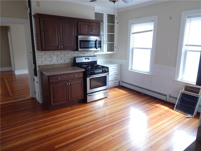 kitchen with a ceiling fan, wainscoting, light wood-style floors, stainless steel appliances, and light countertops