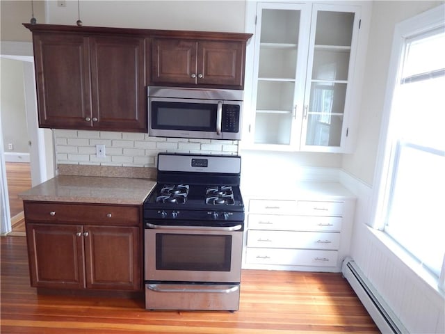kitchen featuring a baseboard radiator, decorative backsplash, appliances with stainless steel finishes, and light wood-style flooring