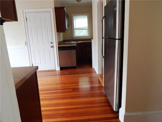 kitchen featuring stainless steel appliances, a sink, dark brown cabinets, wood finished floors, and crown molding