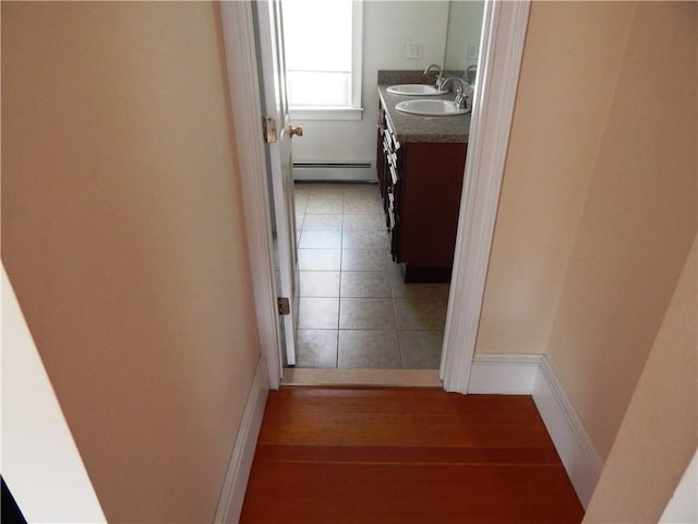 corridor featuring baseboard heating, baseboards, and a sink