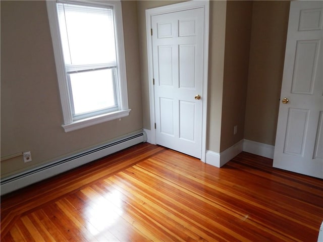 unfurnished bedroom with a baseboard heating unit, light wood finished floors, and baseboards
