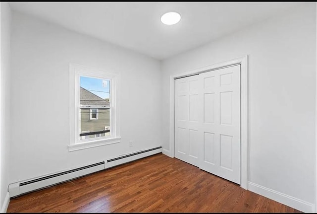 unfurnished bedroom featuring dark wood finished floors, a baseboard radiator, baseboards, and a closet