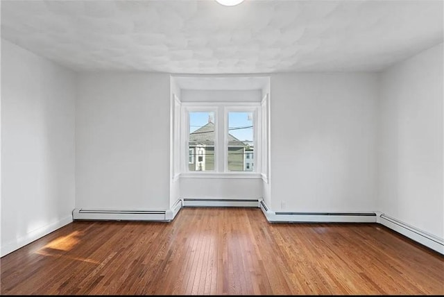 spare room with wood finished floors, baseboards, and baseboard heating